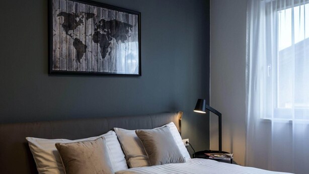A neatly made bed with pillows, a world map artwork on the wall, a bedside lamp, and a window with sheer curtains. - Family apartment in Schwaz (Schwaz)