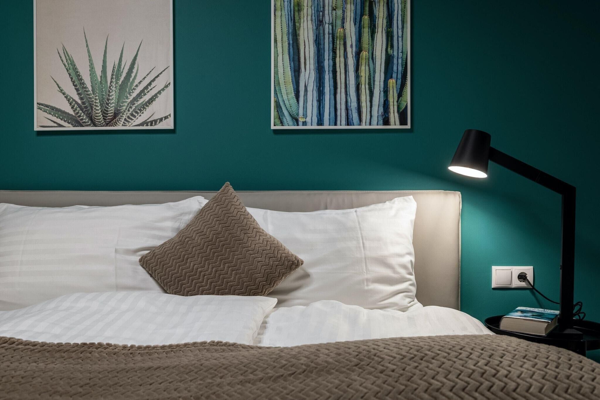 Uma cama bem arrumada com roupa de cama branca e um cobertor marrom texturizado, um único travesseiro marrom e uma luminária de mesa preta em uma mesinha de cabeceira ao lado da cama.
