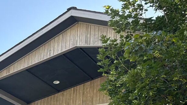 Une maison moderne à deux étages, dotée d’un balcon, de grandes fenêtres et d’un arbre au premier plan.