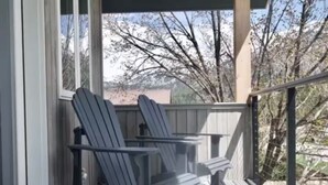 Une véranda abritée avec deux fauteuils Adirondack et une vue sur des arbres et un bâtiment au loin.