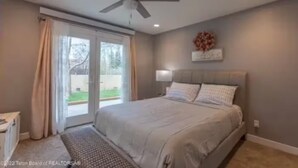 Une chambre à coucher avec un lit, un ventilateur de plafond, une fenêtre avec des rideaux et une vue sur l’extérieur.