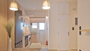 A modern kitchen with wooden cabinets, a built-in oven, and a washing machine. There is a small window and a door leading to another room. - SILIA Reno Studio Athens Ambelokipi Metro (Athens)