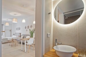 Une salle de bain moderne avec un grand miroir rond, un lavabo blanc et un meuble-lavabo en bois.