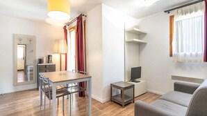 A modern living room with a sofa, a dining table with chairs, a TV, and a small side table.