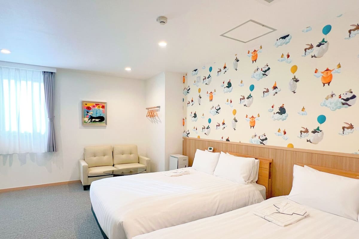 Habitación de hotel con dos camas, un sofá y una pared decorada con motivos de animales.
