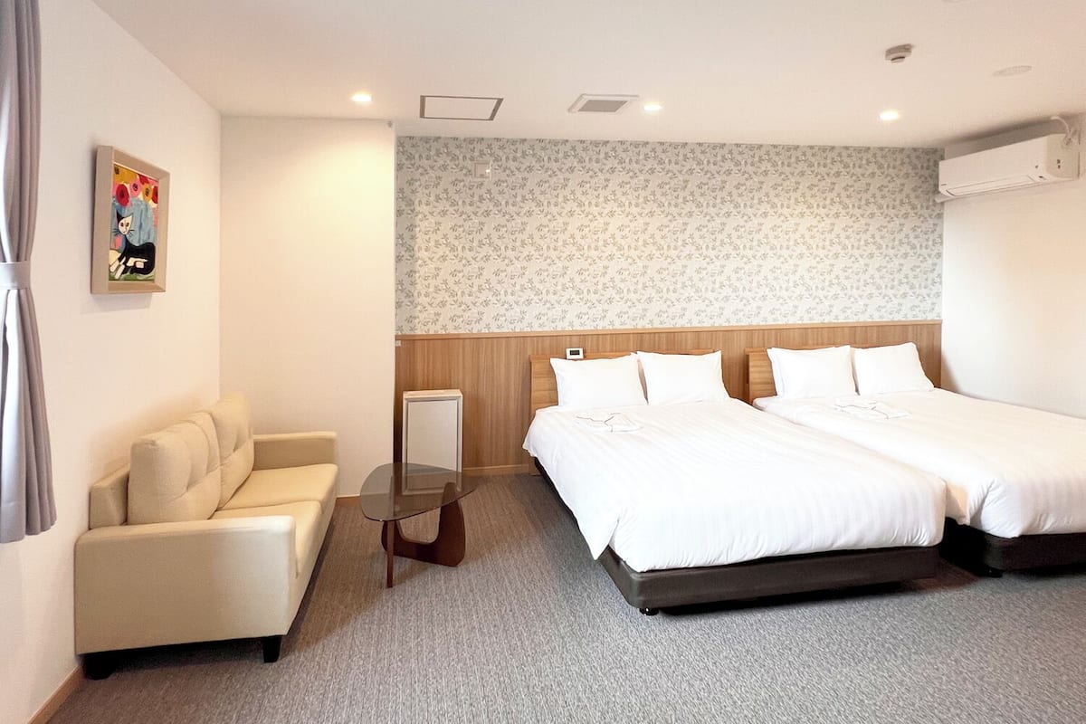 Habitación de hotel con sofá, dos camas, una mesita y papel tapiz floral.