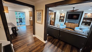 A modern living room with a dark wood floor, a large sectional sofa, a white armchair, and a television.