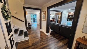 Ein modernes Interieur mit Holzboden, einer Treppe mit weißen und schwarzen Akzenten und Blick in einen Essbereich, durch einen offenen Durchgang zur sichtbaren Küche.
