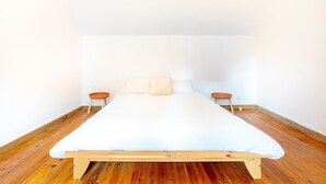 Ein Bett mit Holzrahmen und weißer Bettwäsche in einem Zimmer mit Holzboden und weißen Wänden.
