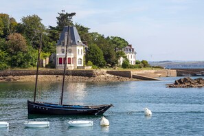 Een kustlandschap met een huis, een zeilboot en een boei in het water.