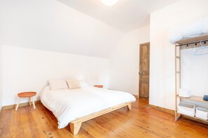Een slaapkamer met een houten bed, een houten garderobe en een klein krukje.