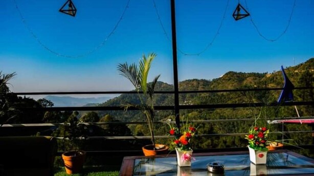 A terrace with a clear view of a mountainous landscape, potted plants, and hanging lights. - Sumangalam Homestay (Pauri)
