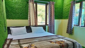 A bed with a floral-patterned bedspread, two pillows, and a window with curtains. - Sumangalam Homestay (Pauri)