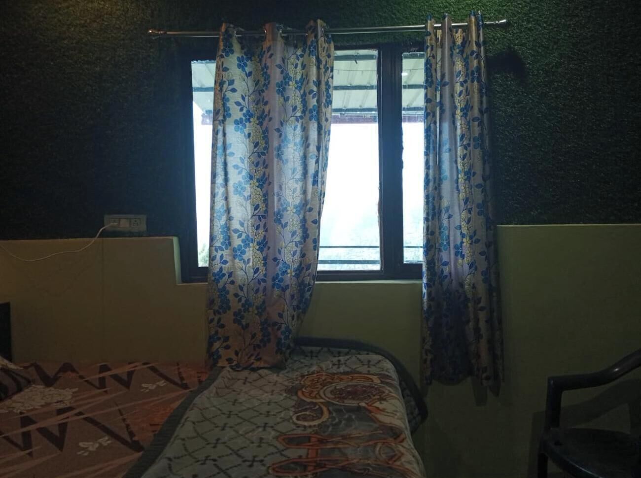 Une pièce avec un lit, une fenêtre ornée de rideaux à motifs et une chaise.