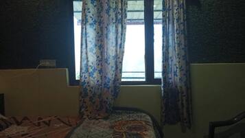 Une pièce avec un lit, une fenêtre ornée de rideaux à motifs et une chaise.