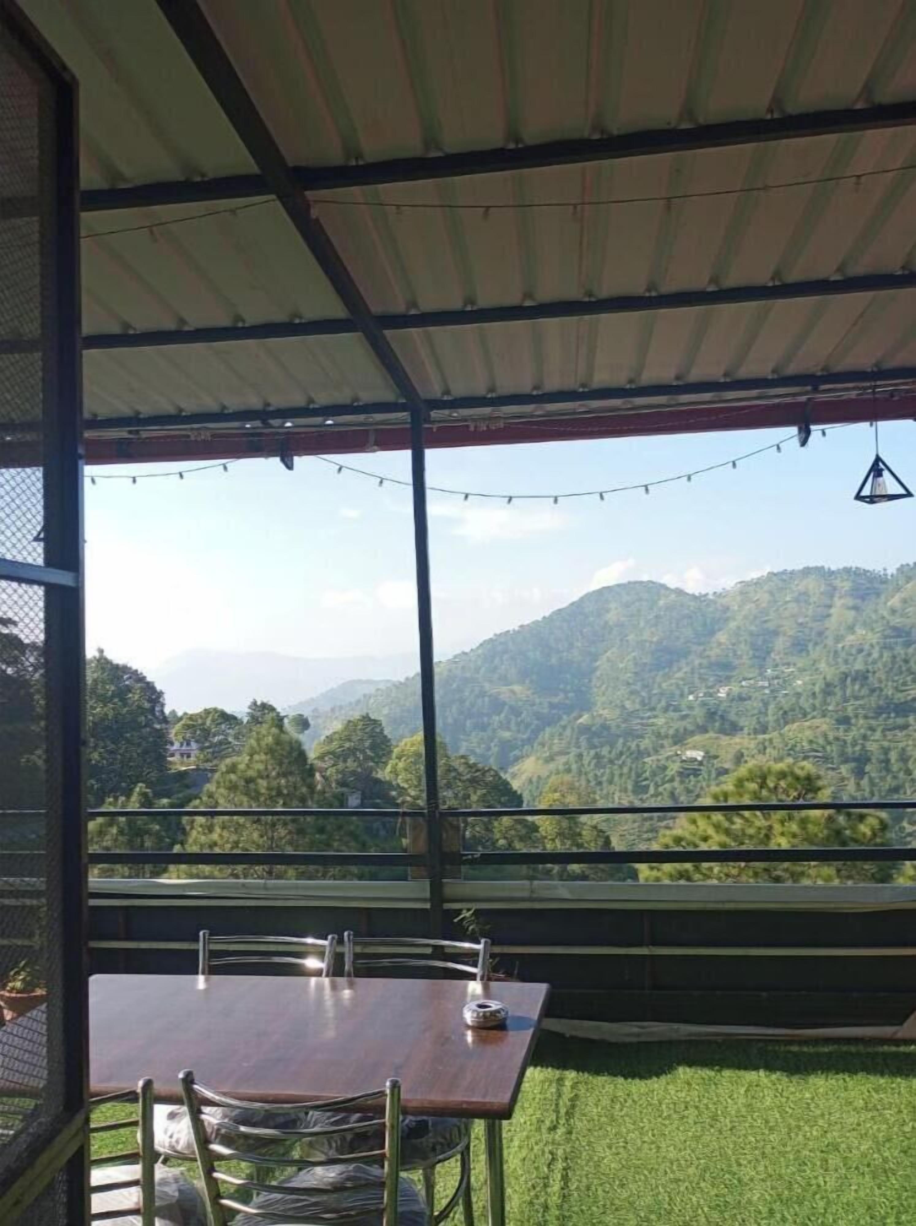 Un espace extérieur abrité, aménagé pour les repas, avec une table et des chaises, offrant une vue sur un paysage montagneux.