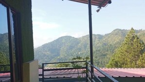 A balcony with a view of green hills, a potted plant, and a metal railing. - Sumangalam Homestay (Pauri)