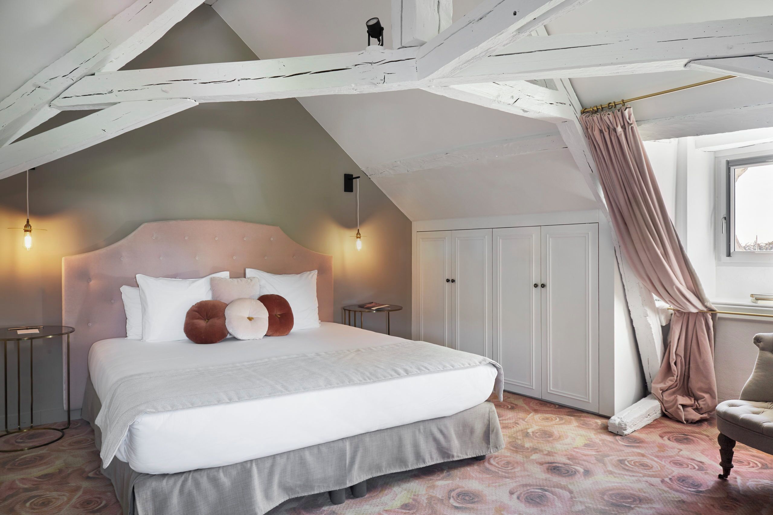Ein Schlafzimmer mit einem großen Bett, einem Kleiderschrank, einem Sessel und einem Fenster mit Vorhängen.