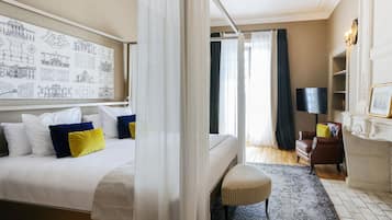 Une chambre d’hôtel avec un grand lit, une table de chevet, une chaise, un bureau, une télévision et un mur orné de dessins d’architecture.