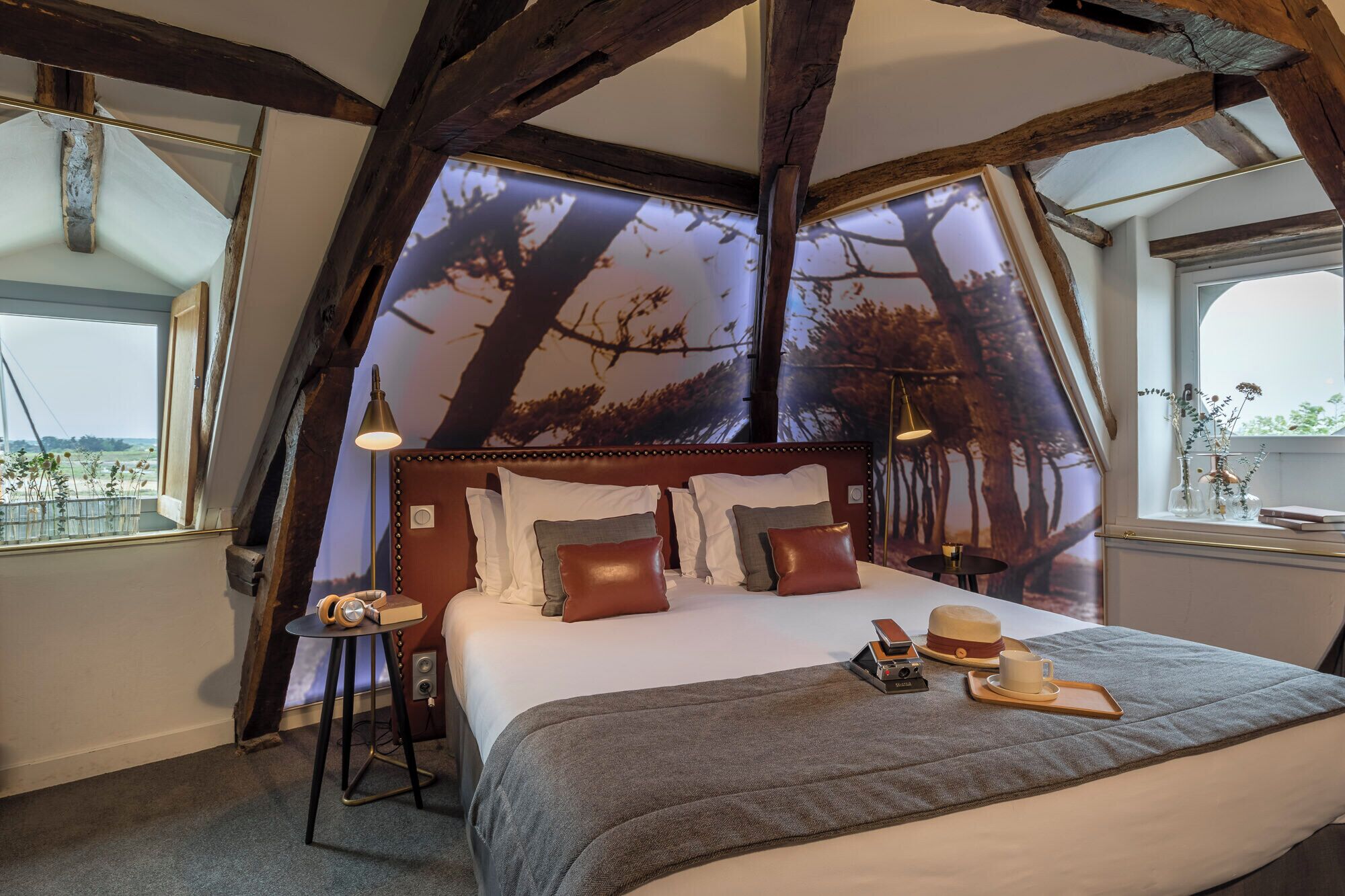 Un dormitorio acogedor con una cama grande, una mesita de noche, una lámpara y vistas a árboles por la ventana.