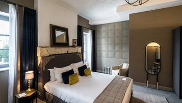 Quarto de hotel com uma cama grande, mesa de cabeceira com abajur, uma cadeira, espelho e painel texturizado na parede.
