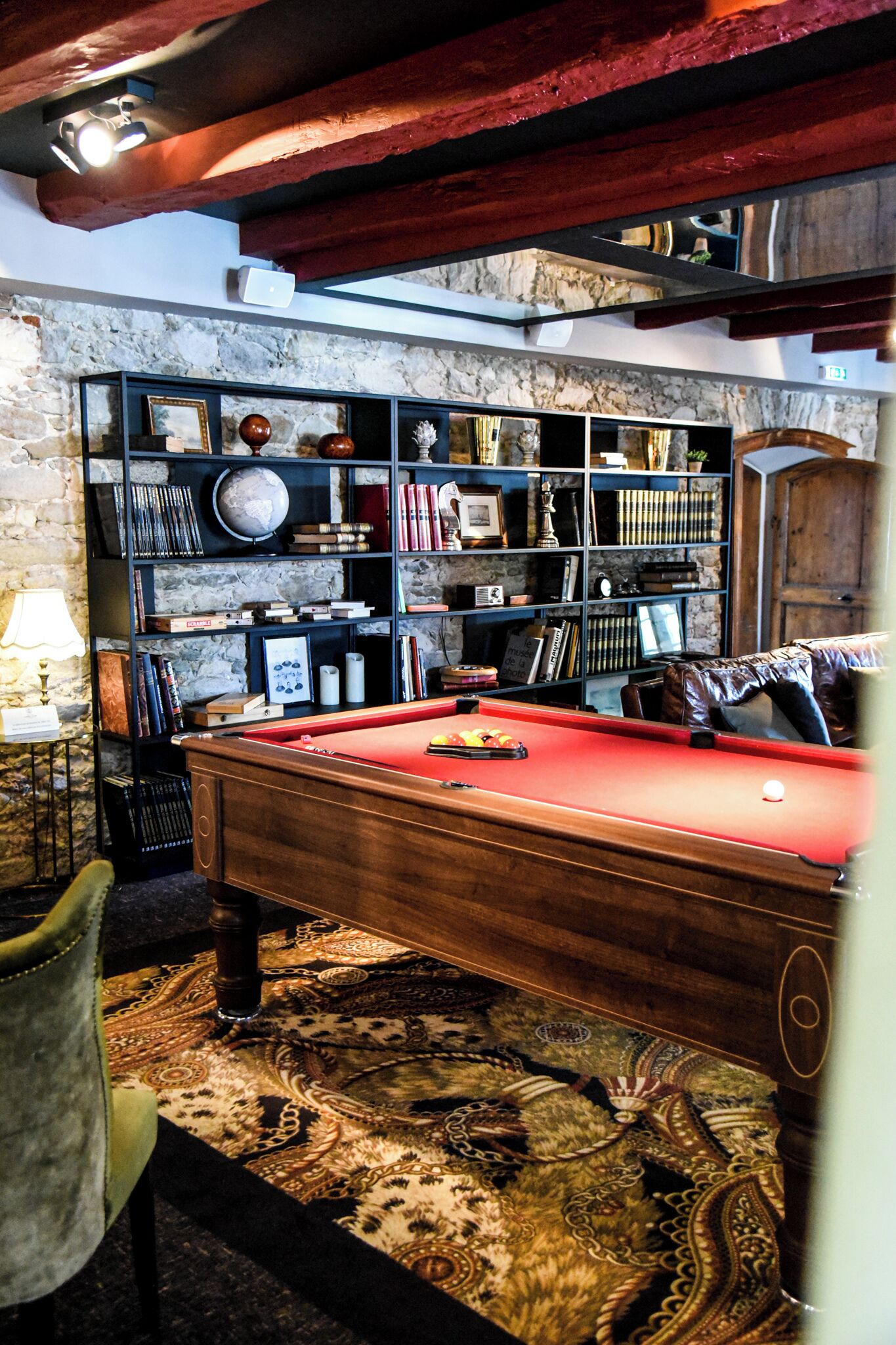 A pool table in a room with a stone wall, a bookshelf with various items, and a leather couch.