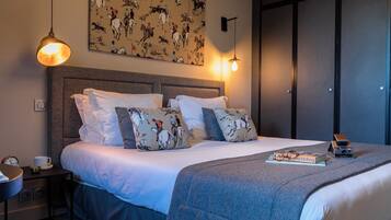 A neatly made bed with patterned pillows, a bedside table with a cup and a book, and a wall with a horse-themed artwork.