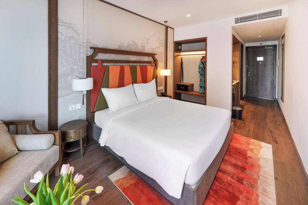 Een hotelkamer met een groot bed, een nachtkastje, een lamp, een spiegel en een houten vloer.