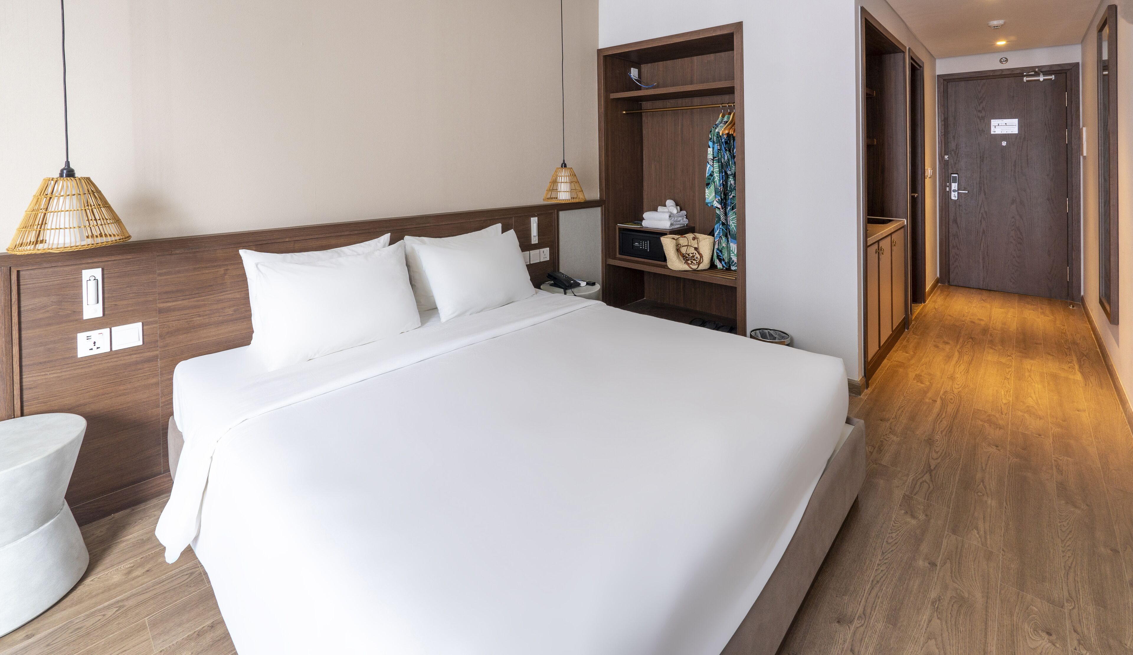 A hotel room with a large bed, wooden headboard, bedside tables, a wardrobe, and a bathroom area.