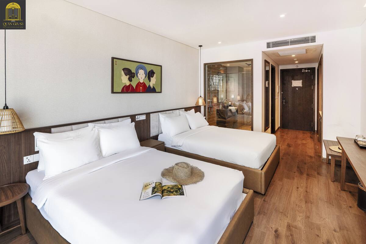 Een hotelkamer met twee bedden, een houten vloer, een schilderij aan de wand en een deur naar een badkamer.