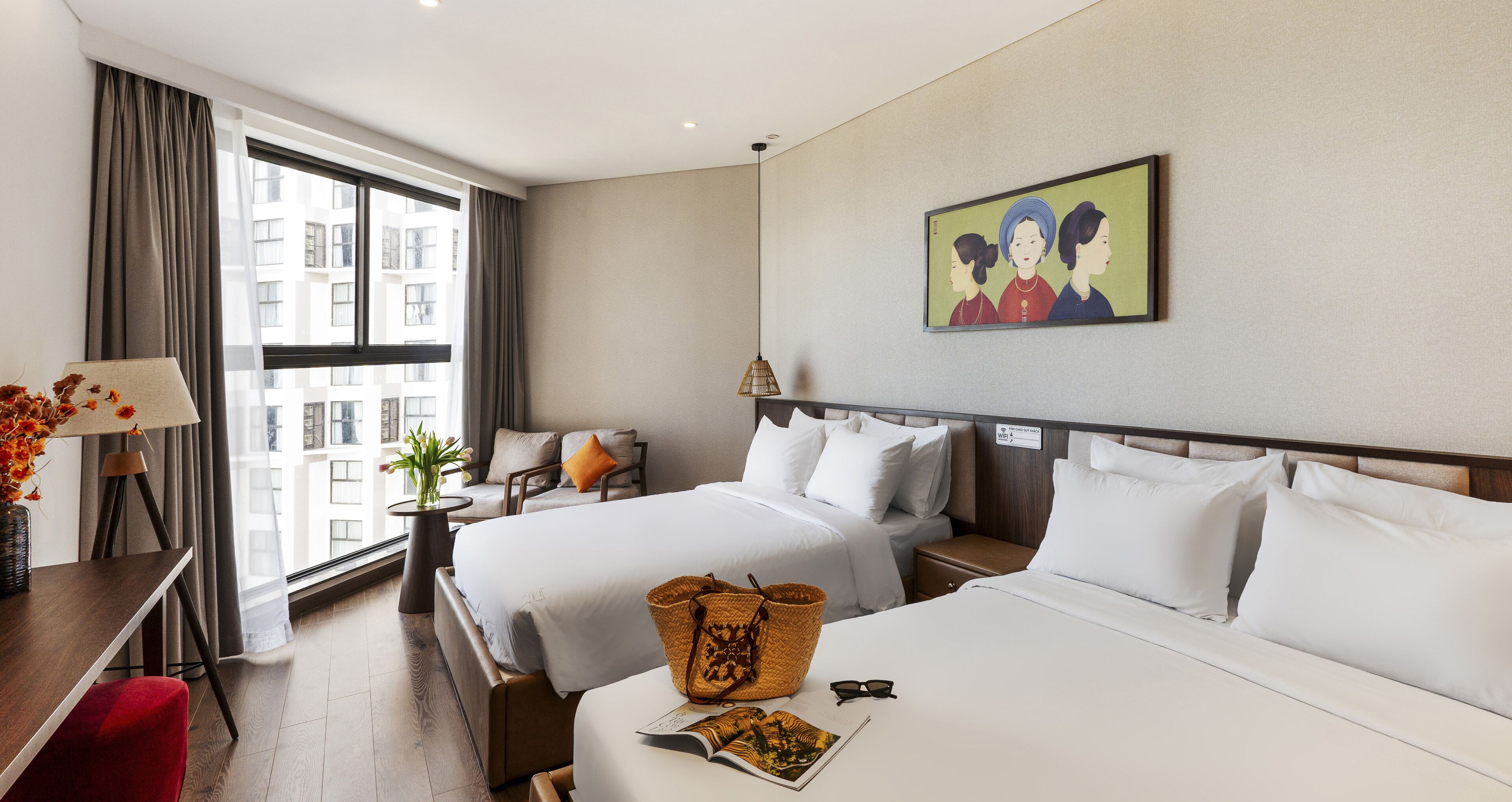 A hotel room with two beds, a desk, a chair, a lamp, and a painting on the wall.