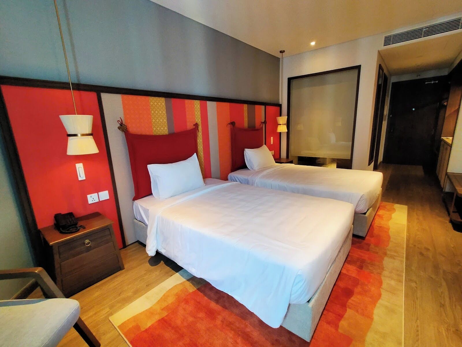 A hotel room with two beds, a nightstand, a chair, and a large window.