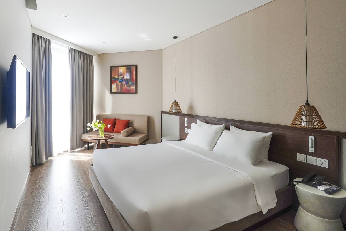 Een hotelkamer met een groot bed, een bank, een bijzettafeltje met bloemen, een schilderij aan de muur en een telefoon naast het bed.