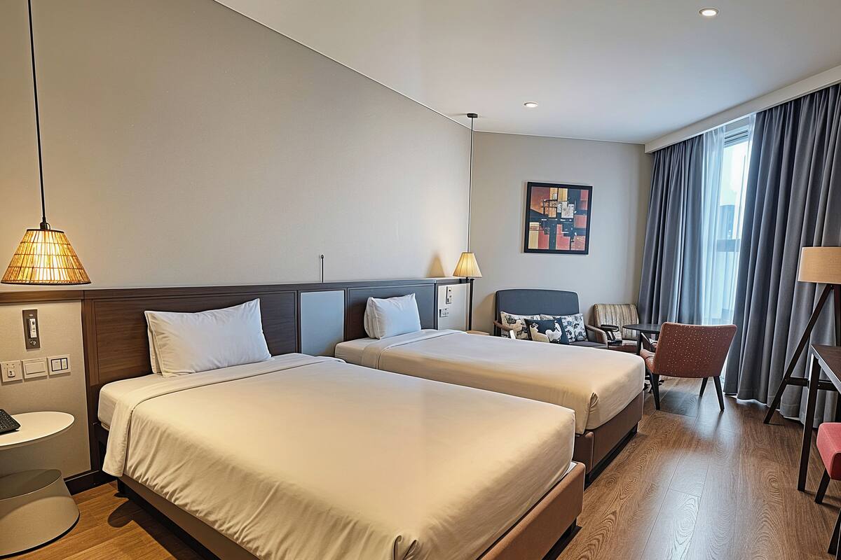 Een hotelkamer met twee bedden, een bureau, een stoel en een groot raam met gordijnen.