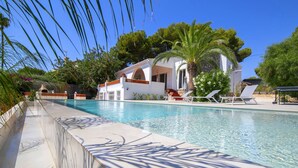 A pool with clear water, surrounded by a white building with a red roof, palm trees, and a clear blue sky. - El Retiro by Interhome (Calpe/Calp)