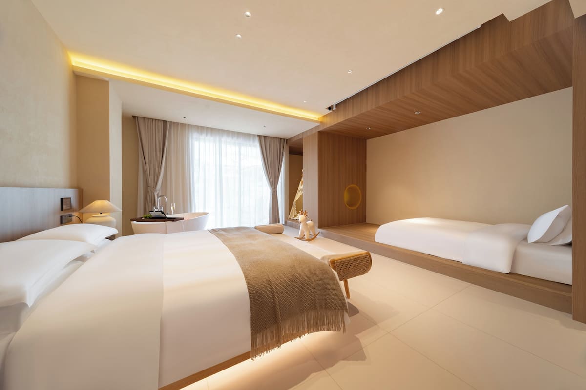 Moderni hotellihuone, jossa on suuri sänky, pienempi sohva, työpöytä ja näkymä kaupunkiin.