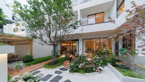 A modern building with a garden area featuring a wooden deck, seating, and various plants. - Warm Shore (Chengdu)