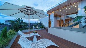 A wooden deck with a white lounge chair and a large umbrella, a small table with fruit, and a staircase with a glass railing. - Warm Shore (Chengdu)