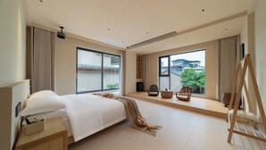 A modern hotel room with a large bed, a wooden nightstand, a desk, and a window with a view of buildings and greenery. - Warm Shore (Chengdu)