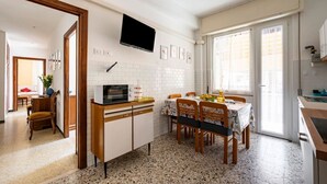 A compact kitchen with a dining area, a TV mounted on the wall, and a window with curtains. - GuestHost - Casa Bina (La Spezia)
