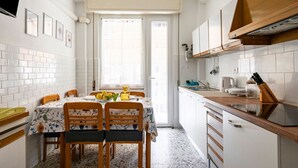 A compact kitchen with white cabinets, a wooden countertop, and a dining area with a table set for two. - GuestHost - Casa Bina (La Spezia)