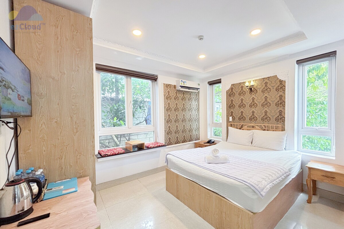 Una habitación de hotel con una cama grande, un escritorio de madera, un televisor y ventanas con vistas a zonas verdes.