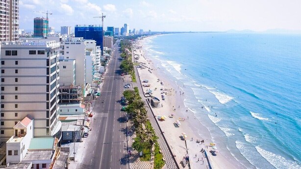 Un paisaje urbano costero con una playa extensa, una carretera paralela a la orilla y edificios altos al fondo.