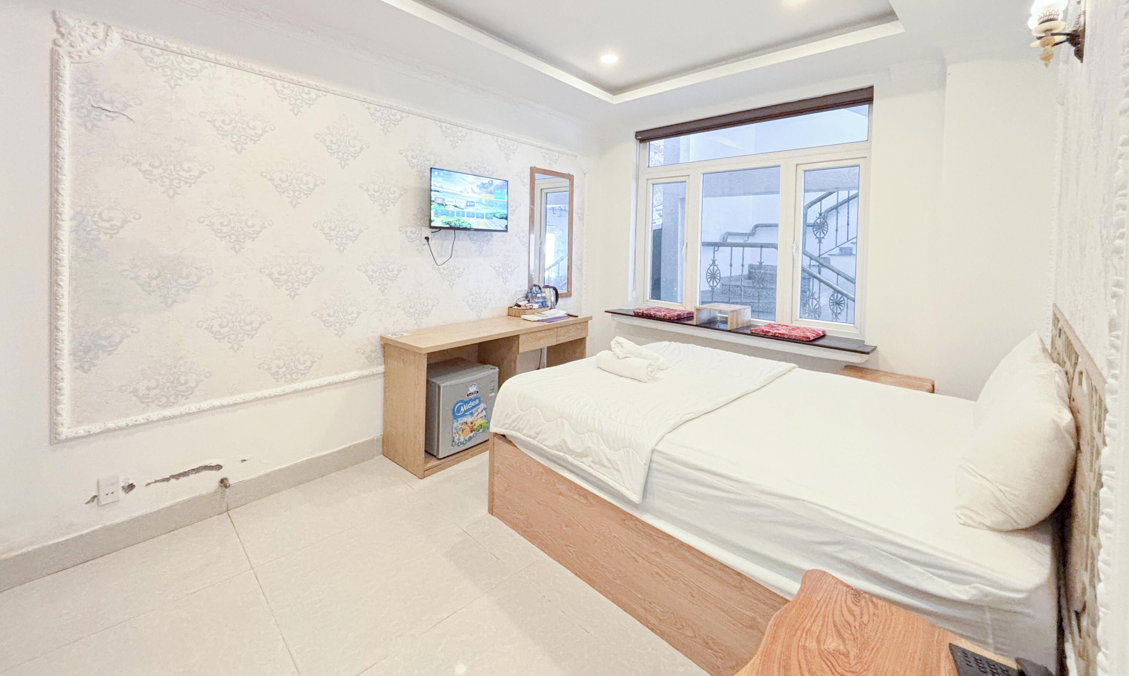 A modern hotel room with a bed, a desk, a television, and a window with a city view.