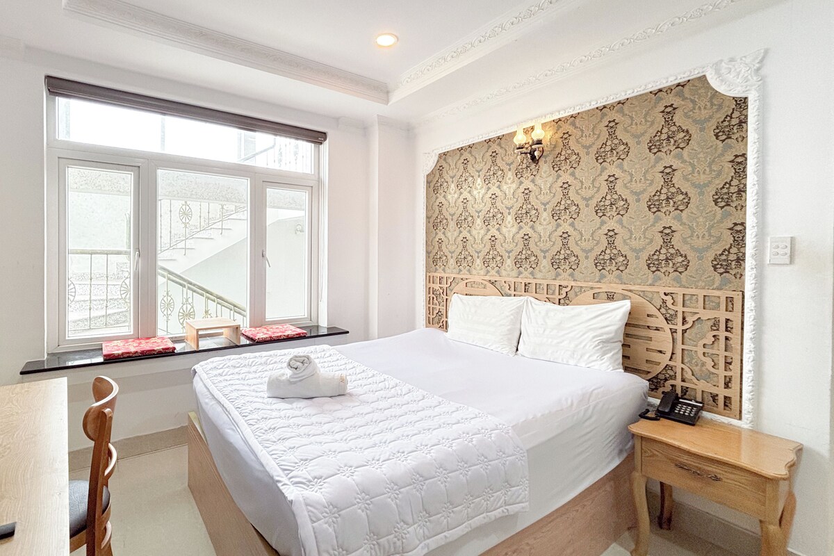Habitación de hotel con una cama grande, un escritorio con silla, una mesita y una ventana que da a una escalera.