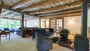 Een rustiek interieur met zichtbare houten balken, een bank, een stoel, een open haard en uitzicht door grote ramen.