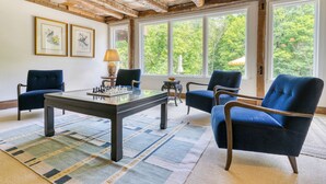 Een kamer met een houten plafond, een schaaktafel en twee blauwe fauteuils.