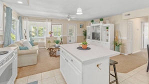 Una cocina moderna con armarios blancos, una isla central y un área de comedor con sofá y mesa.