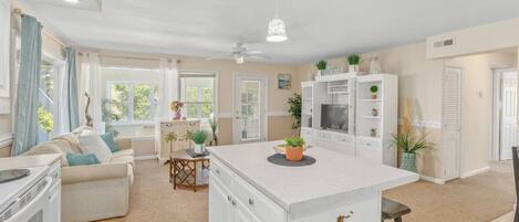 Una cocina moderna con armarios blancos, una isla central y un área de comedor con sofá y mesa.