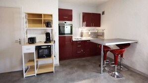 A compact kitchen with a microwave, oven, and sink. There is a small dining area with a table and two red bar stools.